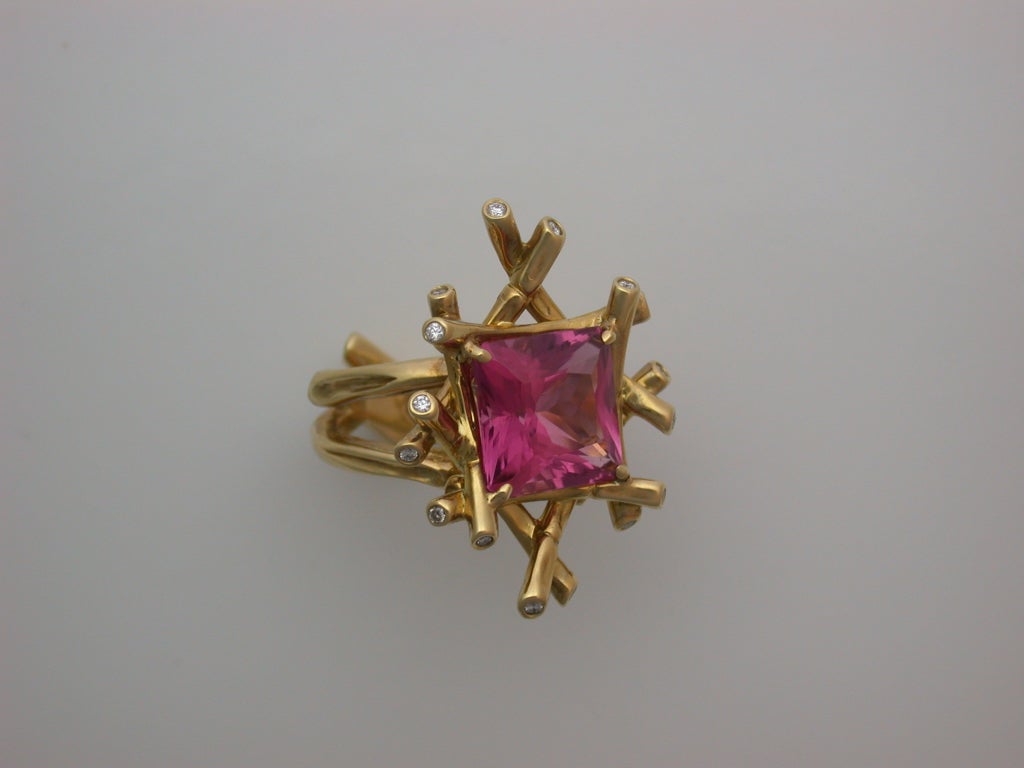 Centering a faceted fantasy square-cut pink tourmaline (a bright candy pink clean stone weighing approximately 7.70 carats) set within a delicate basket of polished yellow gold bamboo canes, enhanced at their tips with round white diamonds