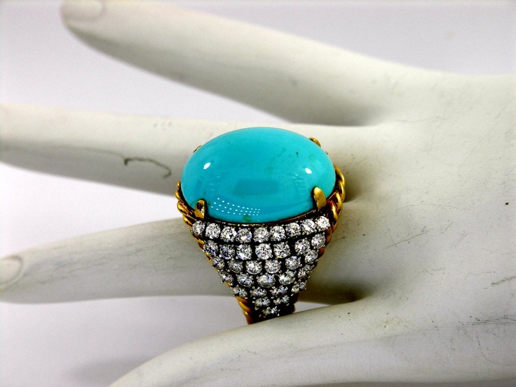 A fine ring in 18K yellow gold set with an oval cabochon turquoise measuring approximately 25mm X 17mm. The sides are set with approximately 5.25ct of assorted G/H color diamonds. The ring rises roughly 5/8 of an inch above the finger, also allowing