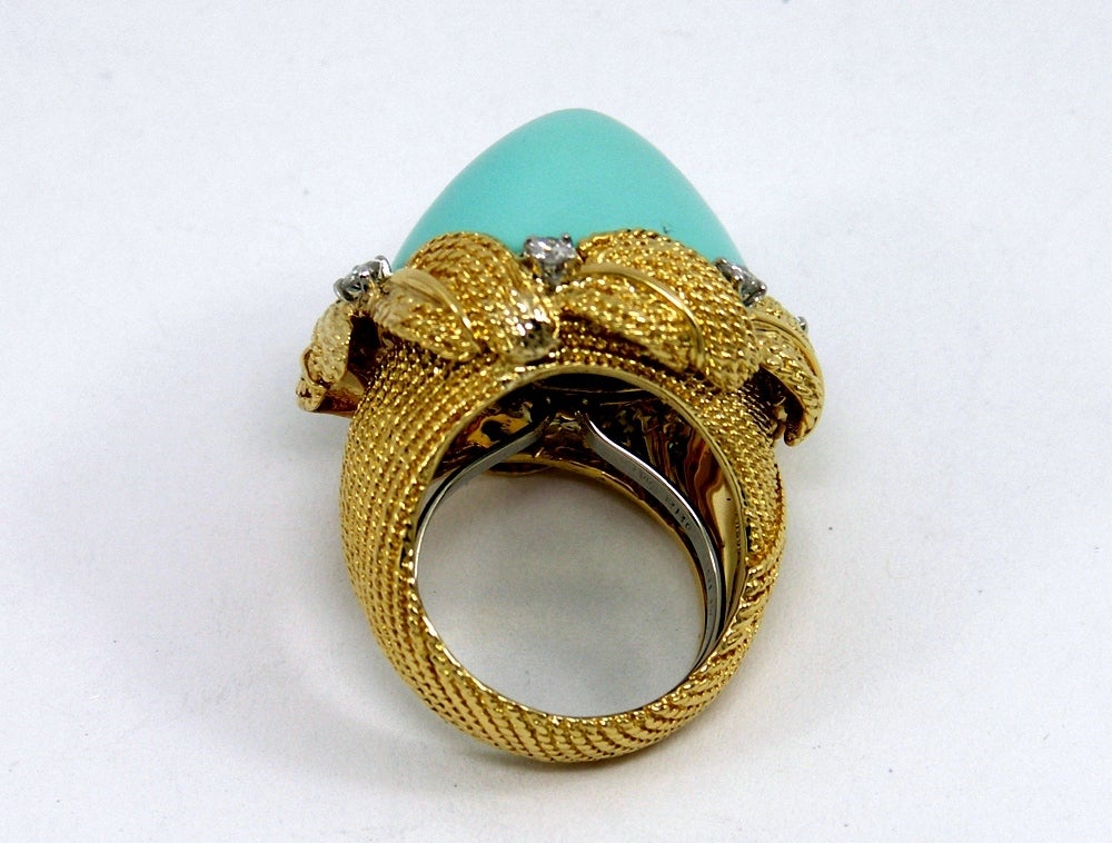 A beautiful ring by David Webb with a twisted rope design in 18K yellow gold. At the center of this gorgeous ring is a high domed turquoise measuring 17mm tall. The turquoise is surrounded by six round brilliant cut diamonds in platinum heads