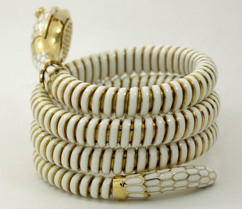 A lady's wristwatch crafted in 18K yellow gold and beautifully detailed with white enamel. With it's serpentine coil, and rounded edges, it can comfortably wrap around wrists from 6 1/2 inches to 7 1/2 inches. The head of the snake features a scale