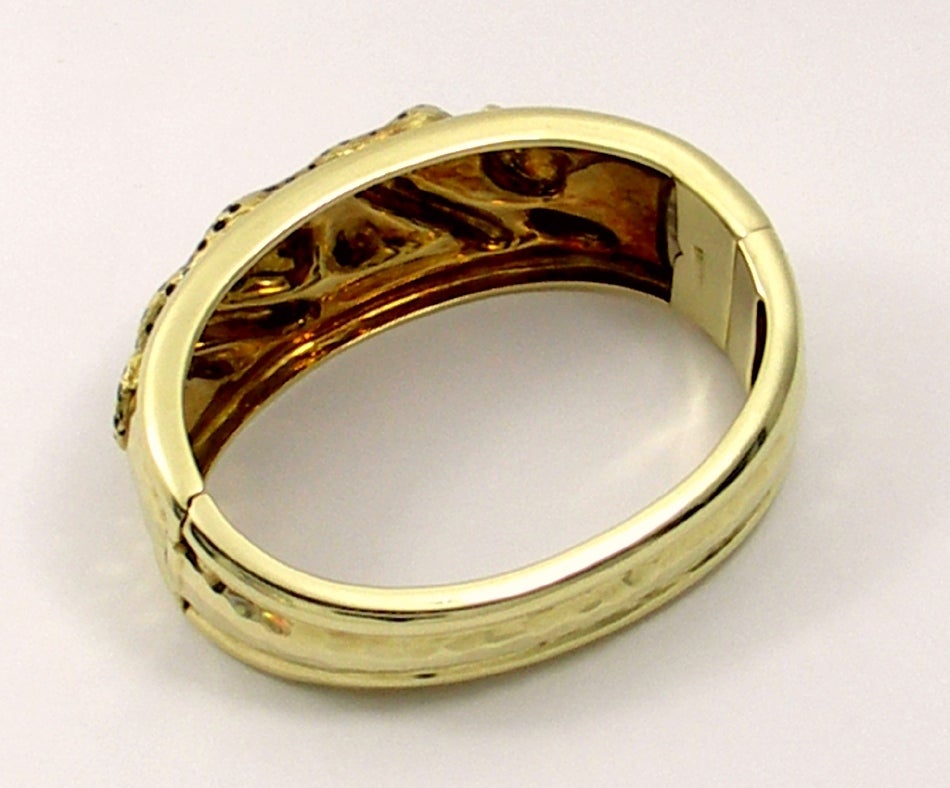 One ladies 18K yellow gold bangle bracelet featuring a cheetah motif with black enamel spots and emerald eye. This bracelet also features a hammer finish as a background along with a high polished edge. It tapers from 1/2 an inch wide to 1 1/4