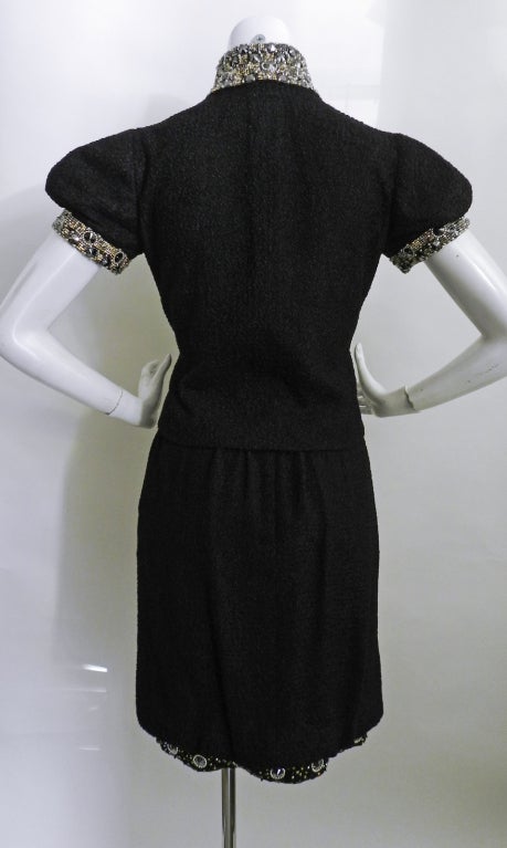 Chanel 08P black boucle wool skirt and jacket suit.  Suit is heavily beaded with glass and crystal at skirt hem, collar, pockets, and cuffs. Jacket has five rhinestone and pearl buttons with CC logos. Lined in silk.  Excellent like-new condition.