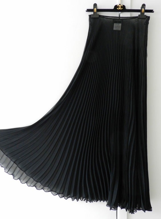 Chanel resort 2002 collection sheer black pleated long column skirt. Side zipper and black metal jeweled CC logo at left hip. Excellent previously owned condition. Tagged size Chanel 38 but maximum waist measurement of 25