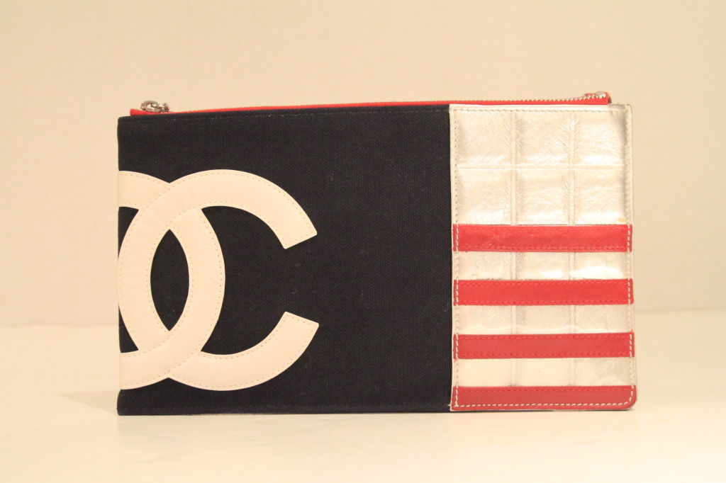 The perfect patriotic addition to any wardrobe!<br />
<br />
<br />
Flag inspired pochette made of navy canvas with red & silver metallic leather trim. White leather CHANEL “CC” logo on front. Top zip closure.  Silvertone chain interlaced with