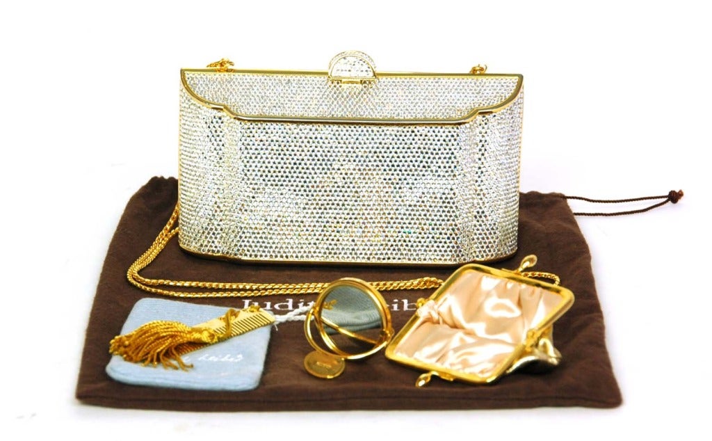 JUDITH LEIBER Silver Crystal Minaudiere Clutch W. Chain

Materials: silver crystals, goldtone metal, gold leather, gold chain strap.
Features angular, oversize minaudiere with silver crystals and gold metal framing. Gold leather 