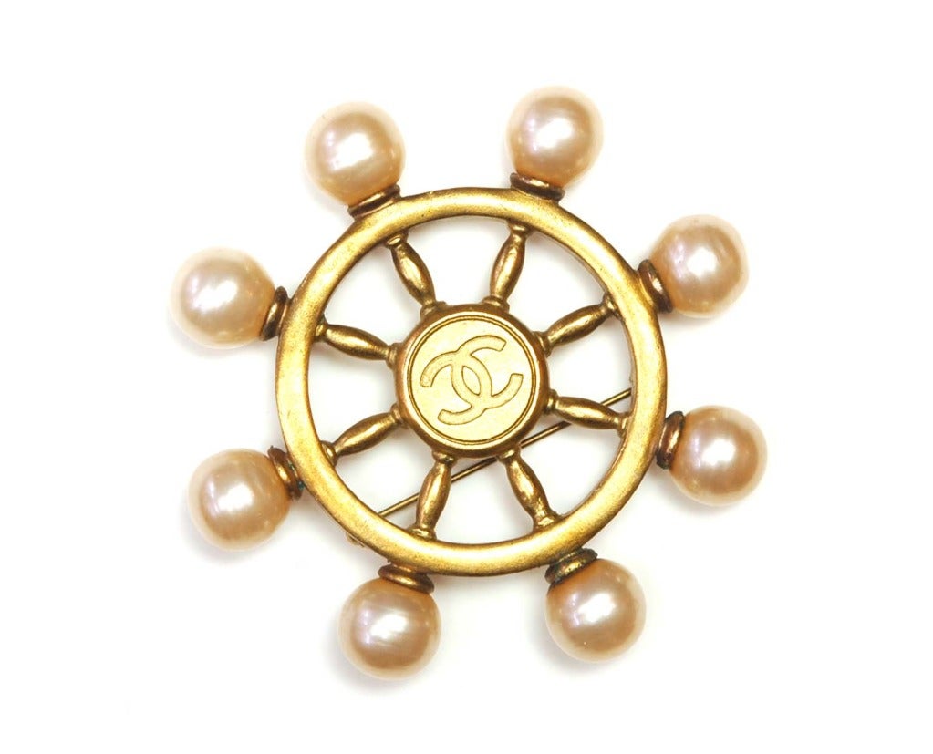 CHANEL Gold & Pearl Logo Ship's Helm Pin

Age: 1994
Made in France
Materials: goldtone metal, faux pearls.
Features goldtone ship's helm with faux pearl accents around the border. Central CC emblem.
Stamped CHANEL 94 P MADE IN