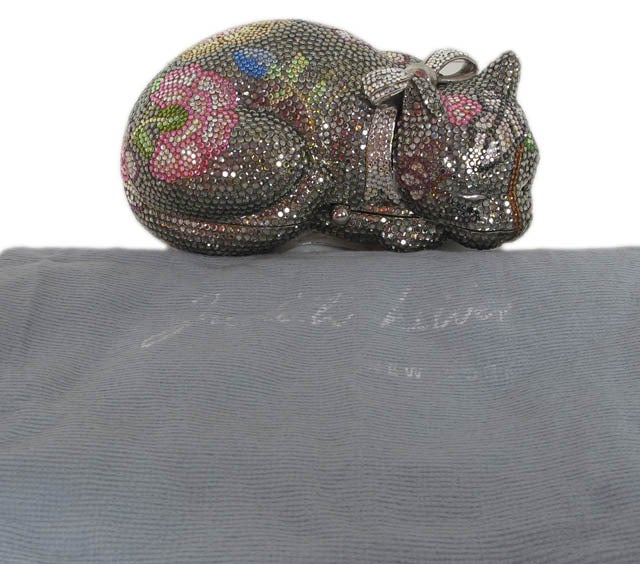 JUDITH LEIBER Floral Swarovski Crystal Sleeping Cat Clutch
Materials: swarovski crystals, silver metal, silver leather.
Features sleeping cat silhouette with floral pattern in swarovski crystals. Cat has a bow around neck. Pushlock closure on