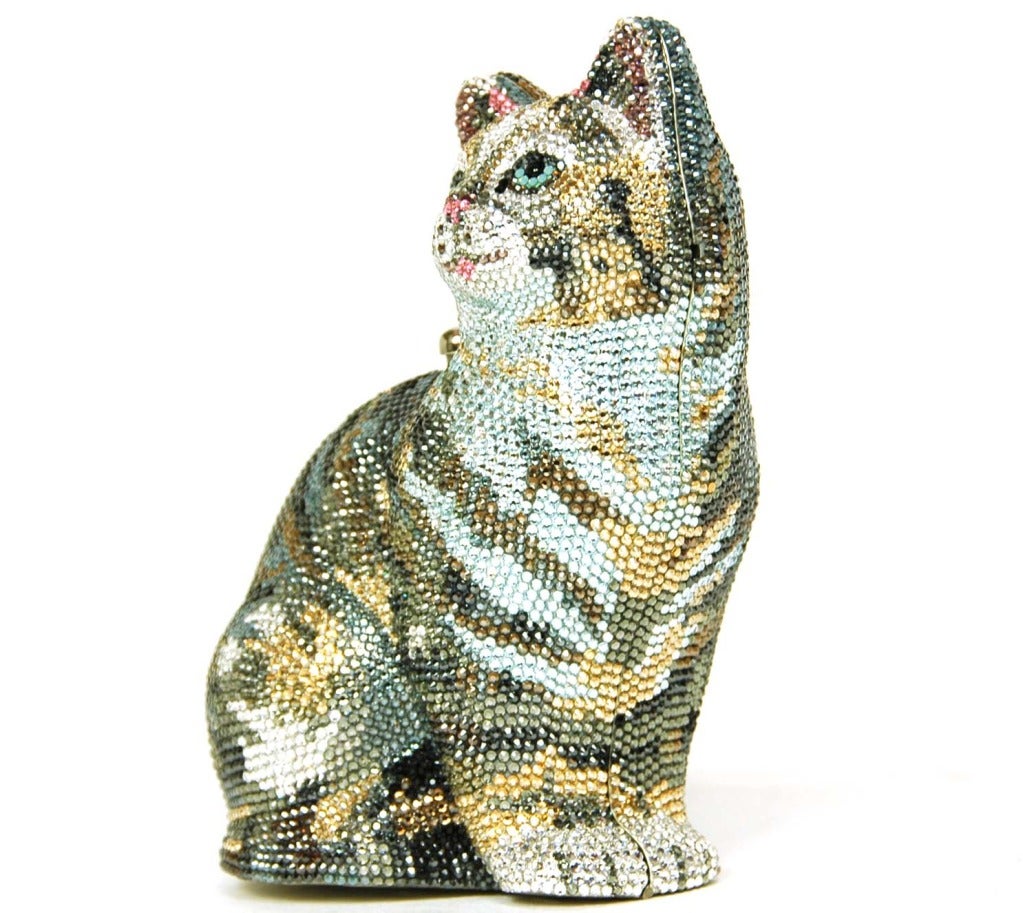 Judith Leiber New in Box crystal cat minaudiere evening bag.
Bag is in the shape of a sitting cat.
Silvertone frame and optional chain strap.
Encrusted in blue, grey, gold, pink, and clear strass crystals.
Base is etched with four paws.
Can be