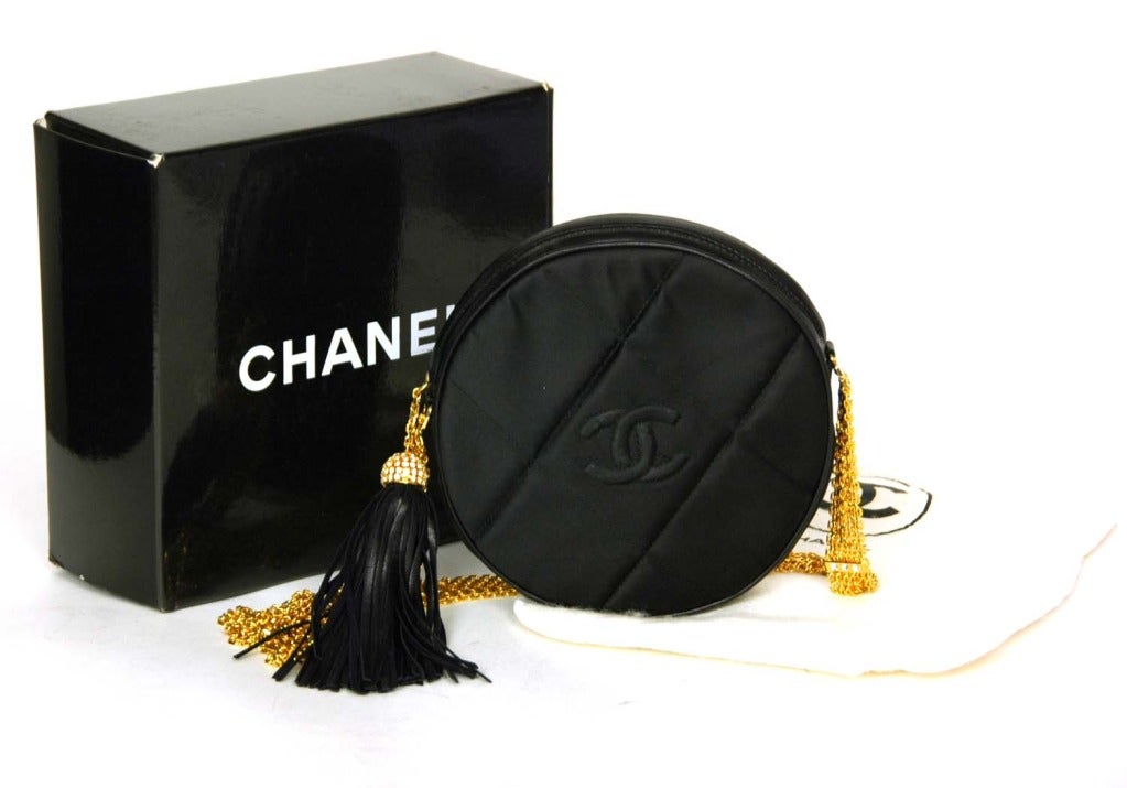 CHANEL Black Satin Circular Quilted Bag W. Gold Chain Strap & Tassel c. 1986
Age: 1986
Made in Italy
Materials: black satin, red leather lining, gold chain strap, rhinestones, black leather tassel.
Features circular quilted satin ziparound pouch