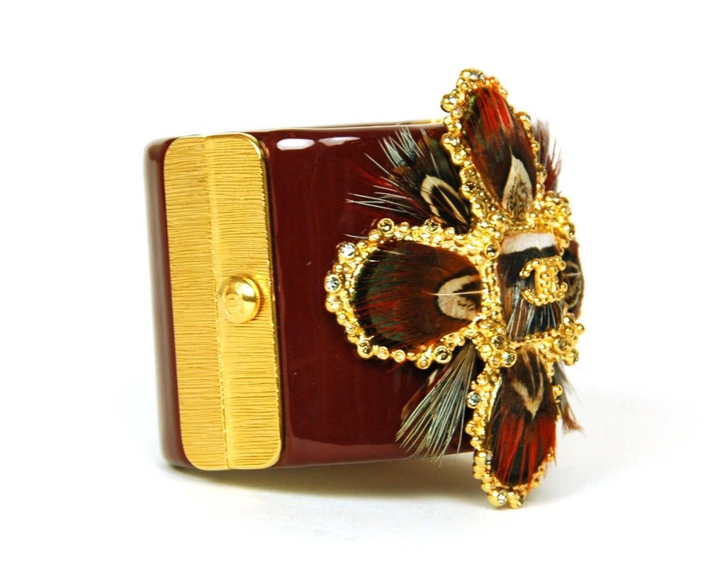 CHANEL Burgundy Resin Clamper Cuff Bracelet W. Logo Feather Medallion c. 2013
Age: 2013
Made in Italy
Materials: resin, feathers, goldtone metal, rhinestones.
Features burgundy red resin cuff with goldtone slide button closure and gold and