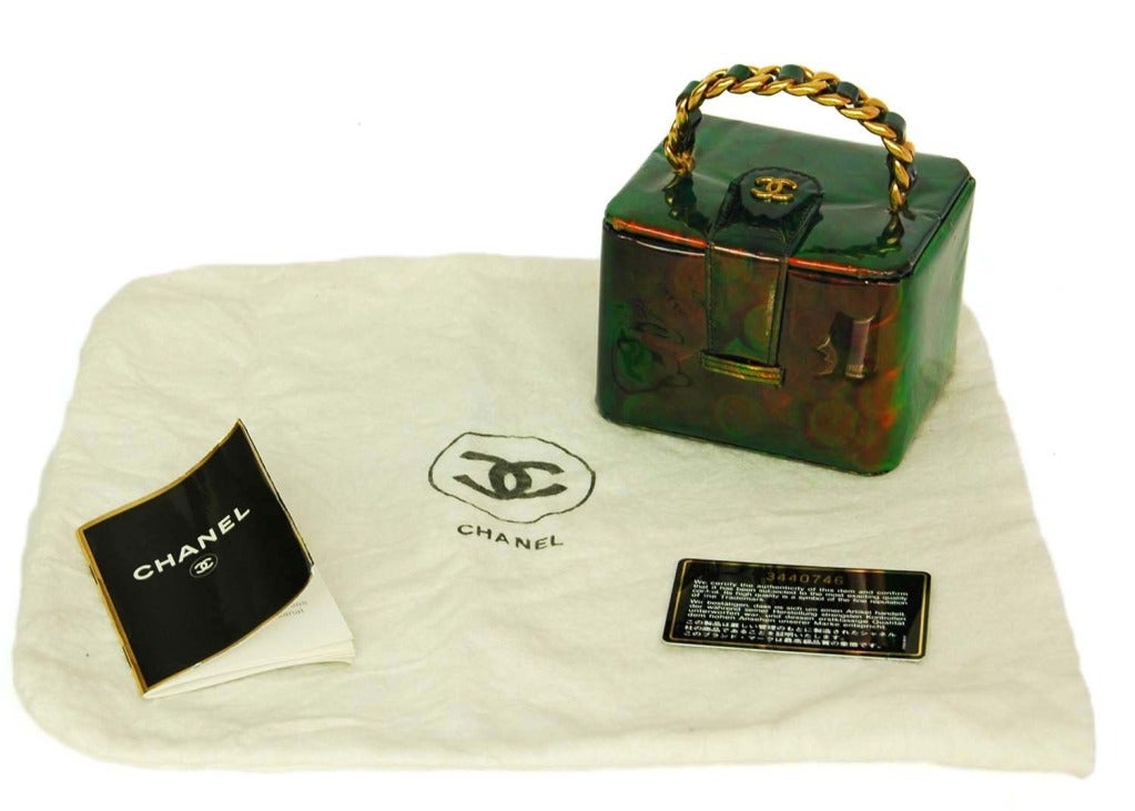 CHANEL Green Hologram Coin Print Box Bag c. 1996
Age: 1996
Made in France
Materials: vinyl, goldtone chain links, black leather, mirror.
Features box shaped bag with flap and snap closure in green hologram coin print. Top handle is vinyl and