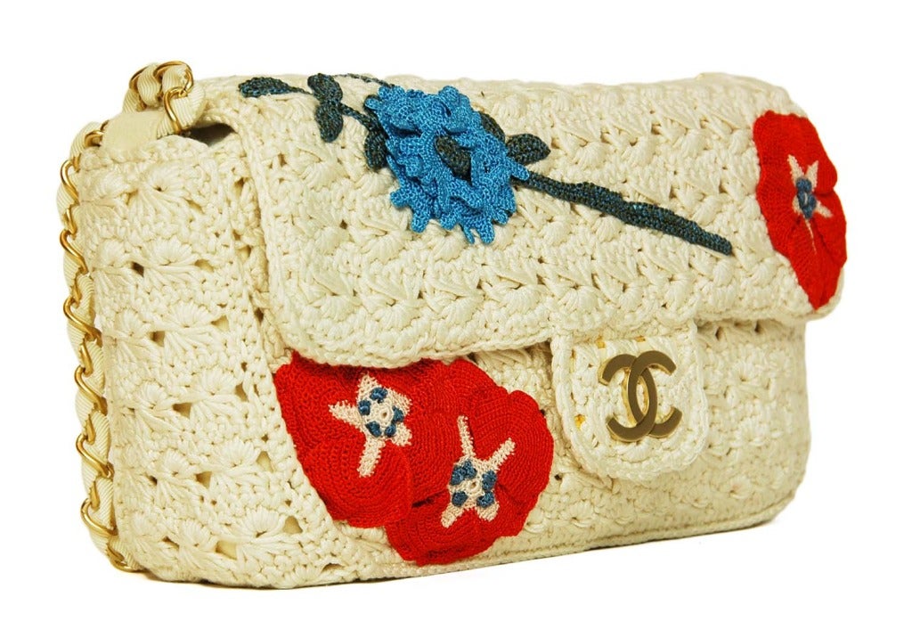 CHANEL Ivory Crochet Floral Runway Flap Bag RT. $4545 c. 2010
Age: 2010
Made in France
Materials: ivory yarn, red blue and pink yarn flower appliques, white suede lining, goldtone hardware, white grosgrain ribbon strap.
Features signature flap