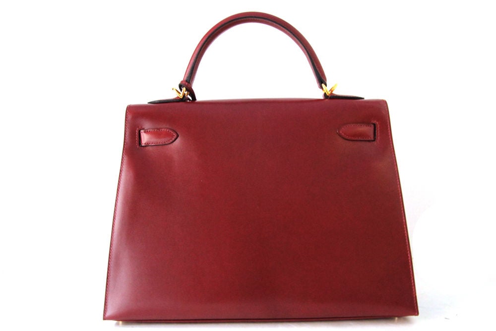 This is a timeless classic HERMES RIGID KELLY bag in a beautiful rouge colorway.  The bag is made in box leather with golden hardware.  Top handle with front flap and twist lock closure.  Inside the bag is lined in full leather, and there a zip