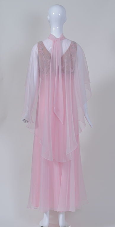 Float through the night in this pale pink evening ensemble. Make your entrance wearing the cape, which flows gracefully over the arms to a longer back and ties at the nape of the neck; through the sheer fabric is a hint of the drama beneath. When