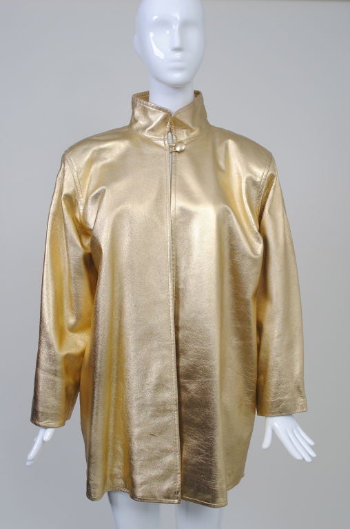 Liven up your wardrobe with this YSL gold leather 1980s thigh-length jacket with Mandarin collar, broad, padded shoulders and dropped armhole. Single button loop closure at neck, double-seam edging. side-slit pockets. Black quilted lining.