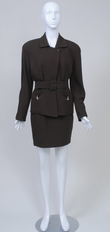 Thierry Mugler 1980s suit in brown wool gabardine features a belted jacket with silver metal stars dangling from the patch pockets and interesting inverted V detail near armhole. Dropped shoulders with pads, curved detail with snap at wrists. jacket