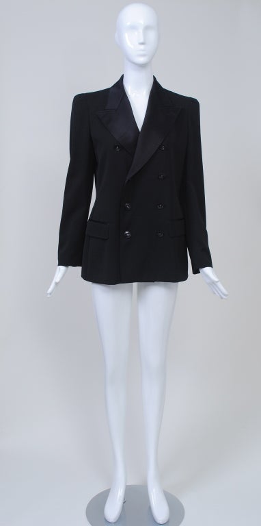 This Jean Paul Gaultier black wool gabardine blazer is double-breasted and has the finish of a tuxedo jacket - wide satin lapels and satin trim over the flap pockets. The long jacket is fitted through the waist and has interesting detailing at the