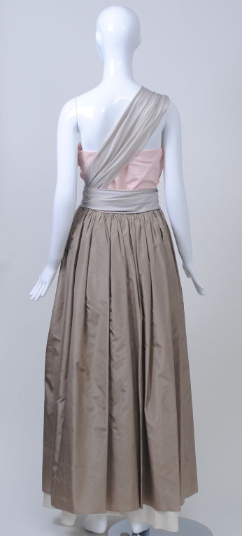 A subtle yet sophisticated palette, as well as a masterful cut, distinguish this Bill Blass gown from the early 1980s. The strapless shell-pink bodice tops a softly gathered taupe skirt; attached to the waist in front is a pale gray piece that