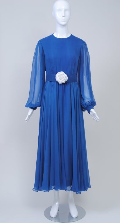 Lovely shade of royal blue in a flowy silk chiffon evening dress with round neck, fitted bodice, sheer full sleeves, and softly draped skirt.  A wide self belt with white flower adds punch. Back zipper, fully lined. By Elinor Simmons for Malcolm