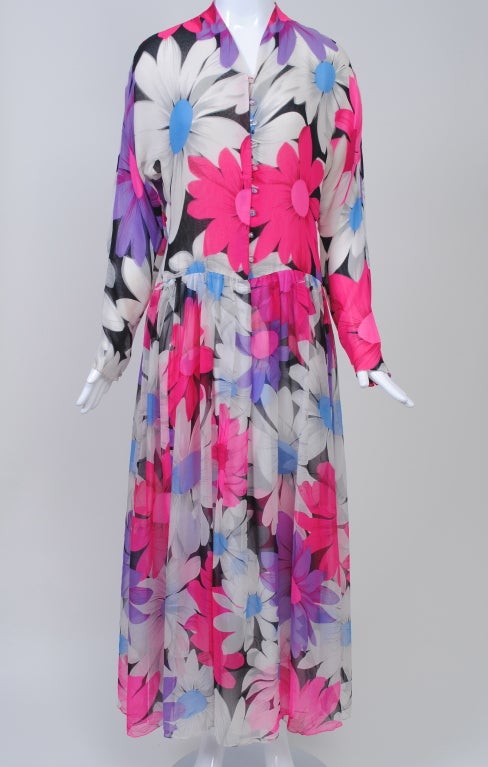 Quintessential Hanae Mori with its vivid floral print, this silk chiffon dress radiates Spring. Enormous daisies in shocking pink, purple, and white overlap on a black ground in a shirt-style cress with long, tapered sleeves and a dropped waist. The