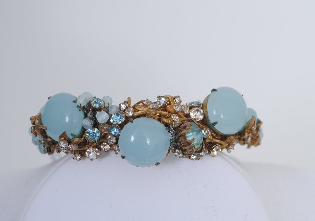One of the best Miriam Haskell bracelets we have seen, this hinged cuff is set with three milky pale blue cabochons and blue and clear crystals set in an elaborate filigree frame, as well as wired pale blue beads in a floral design. The filigree
