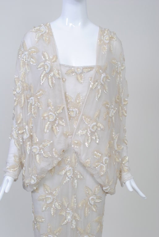 A stunning piece of interesting construction. this sequined long dress makes a dramatic statement. Constructed in one piece of a crinkle white chiffon, the entire piece is studded with large sequin flowers in white and beige. The inner layer is a