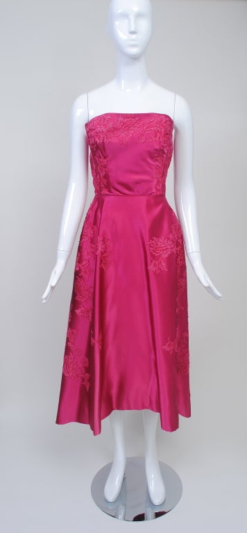 This Harvey Berin evening dress is fashioned of the most beautiful shade of cerise silk satin and is appliquéd with matching lace. The strapless bodice is close fitting with boning on the inside for support. The skirt is cut shorter in front and