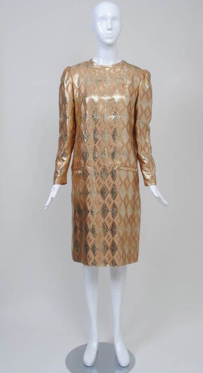 Bill Blass simple long-sleeve sheath in lightweight camel silk woven with metallic gold thread in a diamond pattern. Bound horizontal fake slash pockets and round neckline with snap. Shoulders slightly puffed. Back zipper. Fully lined in silk.