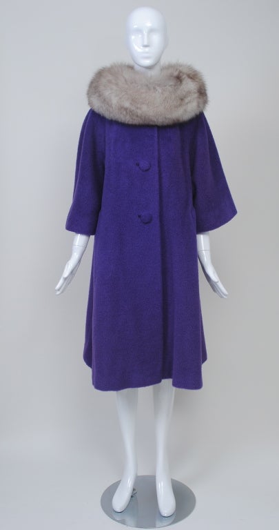 Fabulous color and style define this 1960s Lilli Ann coat. The gray fox cowl collar frames the face of the swing-style coat, which is made of a vibrant purple mohair-type wool. Raglan sleeves allow for movement and the wide three-quarter sleeves