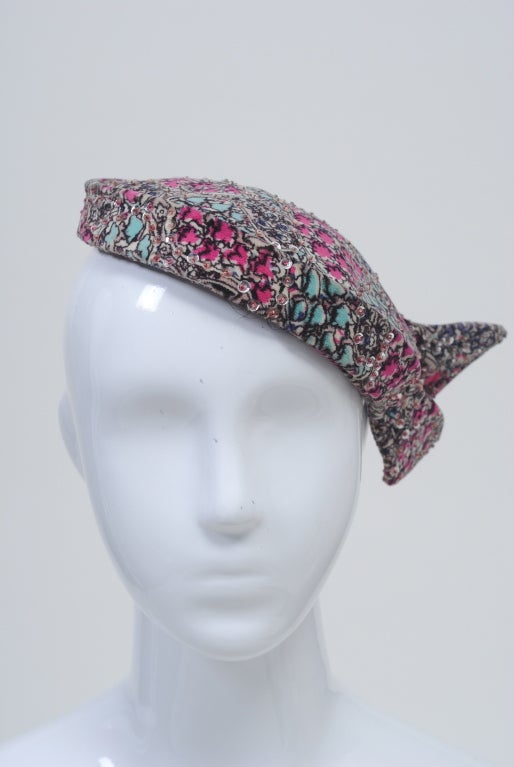 Cappello anni '50 in un bellissimo velluto stampato nei toni dell'acqua e del rosa, ornato da paillettes argentate. Appoggialo in diverse posizioni e fissalo con una spilla da cappello. Etichettato 