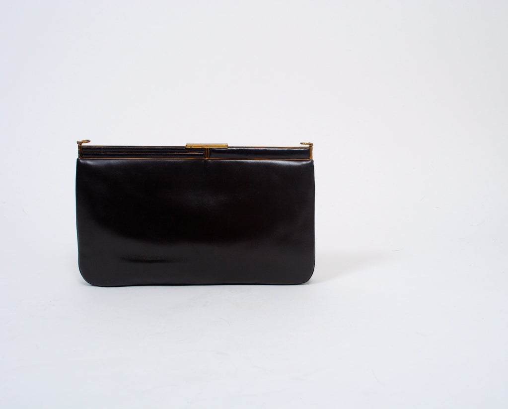 Judith Leiber brown leather convertible clutch is rectangular in shape and has a metal frame and clasp inset with the leather. A detachable narrow leather strap toggles through loops to convert to a shoulder bag. Interior is brown faille with zipper