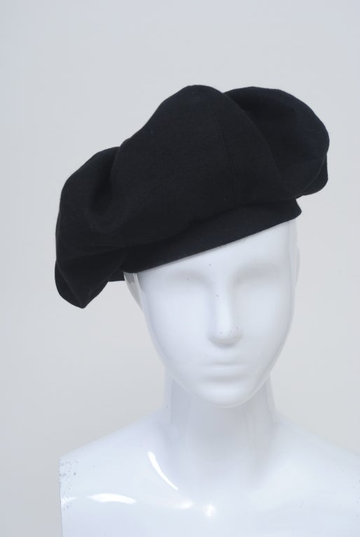 Hattie Carnegie beret in a fine wool felt conposed of seamed and welted gores of the fabric caught on top with a large button and banded around head. Small size.