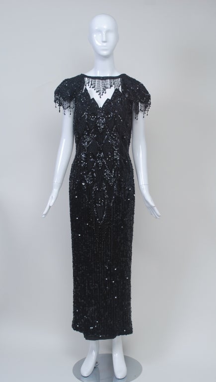 Glamour personified, this gown is beaded throughout with sequins and beads in a geometric pattern that echoes the zigzag lines of the sleeves and neckline. Most distinctive is the beaded fringe on the cap sleeves, the skirt, and around the neckline,