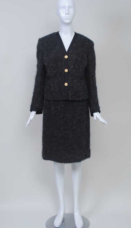 This charcoal mohair suit emulates the style and construction of a Chanel suit c. 1960s. It carries the label Richard Carriére, a company that presumably made faithful reproductions of high-end French clothing. The V-neck jacket is bordered in black