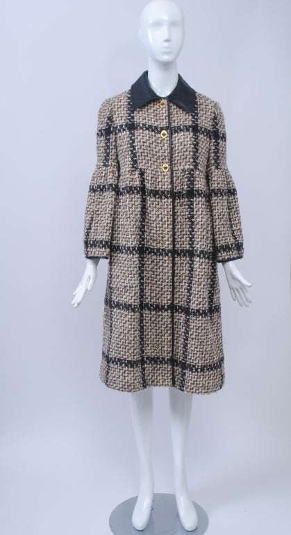 This unmistakeable Bonnie Cashin coat has her signature leather trim and toggle closures, as well as the unusual detail of empire styling and bell sleeves. The fabric is a large-scale plaid of light brown, black, and white. Black leather collar and