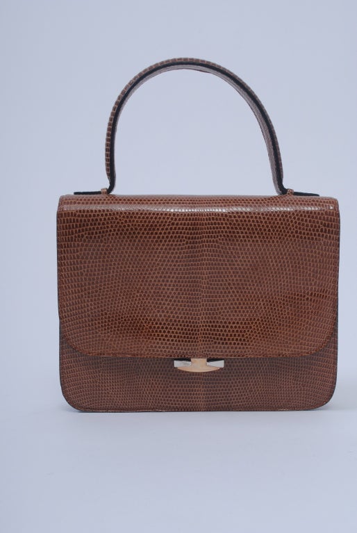 Petite handbag in cocoa lizard with envelope flap and sleek metal push clasp in gold and silver metal. Nice detail on single handle and back flap edge, where two self buttons mark the corners. Interior is divided into two, with zipper and open slots
