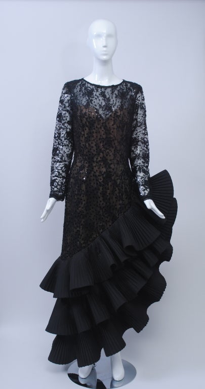 Dramatic evening dress with a Spanish flare from Victor Costa, 1980s. The body is of sheer black lace embellished with sequins and has long sleeves, a round neckline, and a keyhole back; underneath is a nude strapless lining. The defining feature is