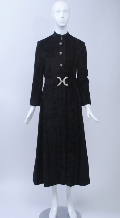 1960s evening coat in black crushed velvet has a neat profile and features a mandarin collar and wide belt. Finished with domed rhinestone buttons and a double-C rhinestone buckle. Petite sizing.