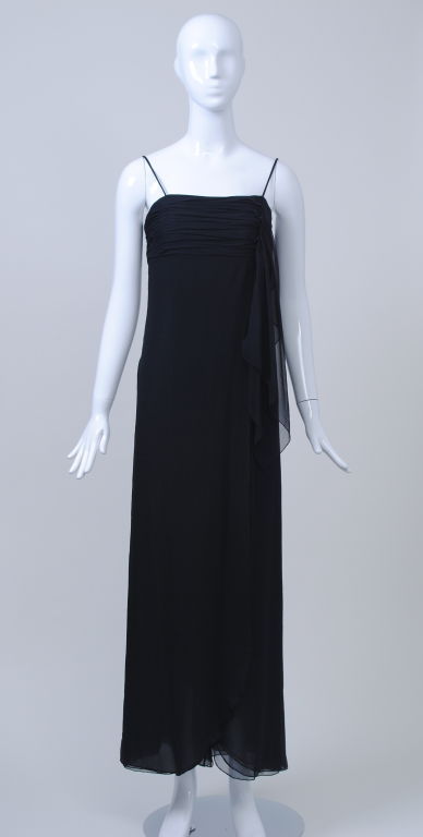 A timeless classic, this Valentino column dress falls just above the ankles. It features a tucked bodice across the bust, spaghetti straps,  and a draped wrap effect that curves at the hem. Several layers of black silk chiffon add softness to this