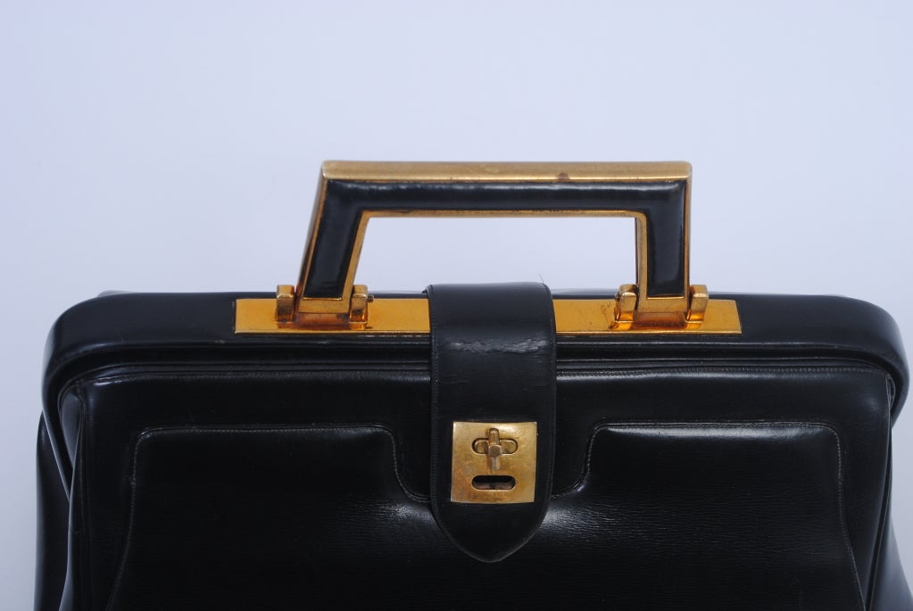 A stunning early Judith Leiber design, this hefty satchel is in black leather with gold tone hardware and features an envelope flap across the front that opens to reveal a slit pocket. The interior is roomy and lined in black faille. Square metal