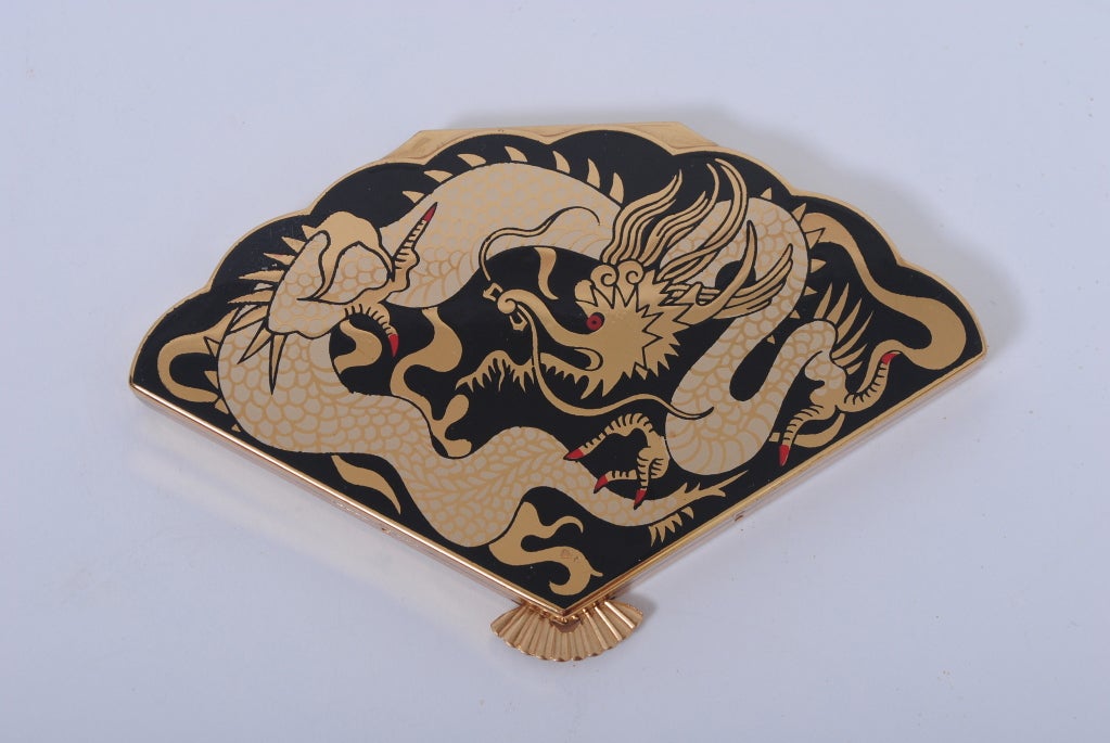 Fan-shaped compact, c. 1950s, with enamel dragon decoration in black with red accents. Opens to mirror and compact compartment. In unused, excellent condition; mirror crazed. Unmarked.