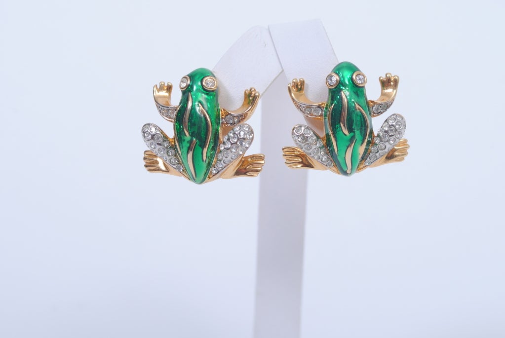 Add a touch of whimsy and joy to your jewelry wardrobe with these frog-shaped earrings by Kenneth Jay Lane.  The frogs, in gold tone metal, have splayed appendages, the body enameled green and the legs and arms studded with pave rhinestones. Eyes