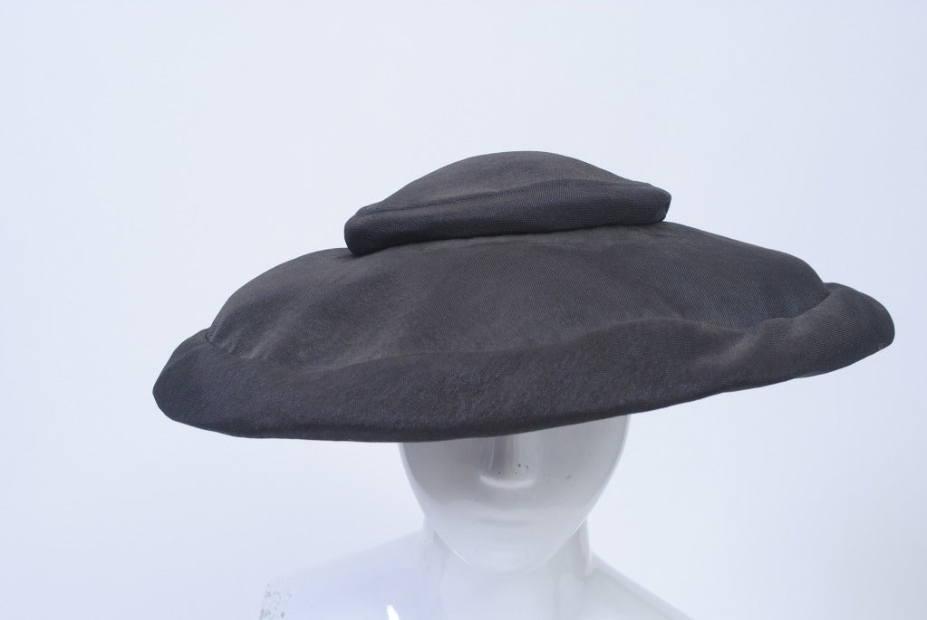 M. John, l'un des plus grands modistes américains, était connu pour ses formes classiques et sans fioritures. Il a travaillé sous sa propre marque de la fin des années 1940 jusqu'en 1970. Ici,  un chapeau-photo en tissu noir légèrement lustré, doté