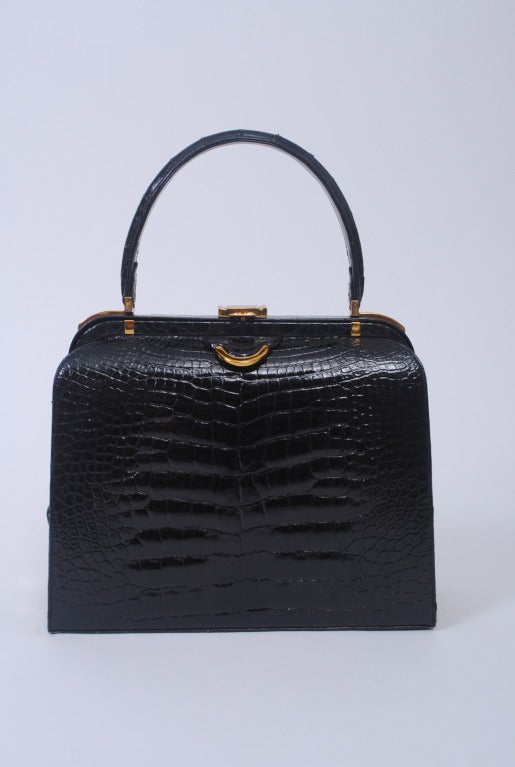 A classic 1960s shape in black alligator that features interesting side detailing and nice goldtone hardware accents, especially at the sides. Single sturdy handle. Clasp lifts to open bag. Black leather interior has multiple side compartments,
