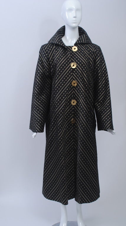 In a larger size, this 1980s coat is quintessential Pauline Trigère - chic simplicity in a beautiful fabric with interesting details. The swing-style coat is constructed of a lightweight, dressy black fabric with gold metallic patterned stripes