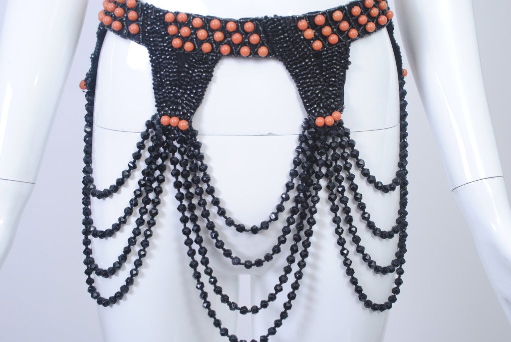 This unique piece of trim from the 1920/'30s can be worn as a neck piece or belt to stunning effect. A band beaded with small black beads and studded with round coral beads suspends three swags of faceted black jet beads, four graduated stands each,