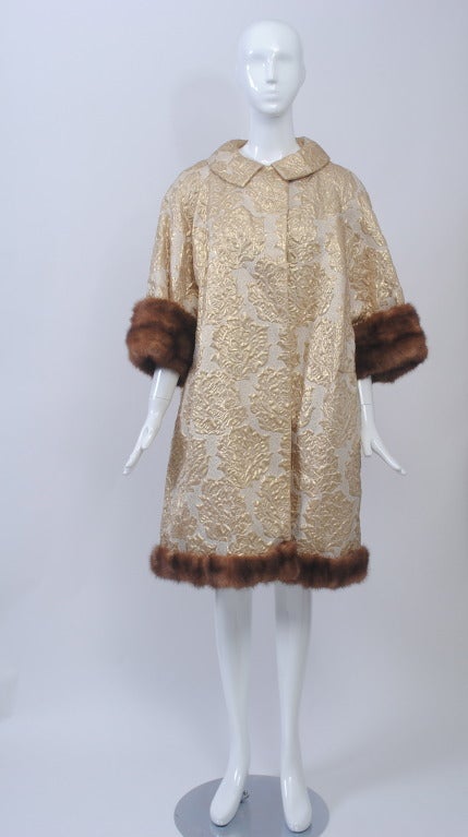 Hard-to-find larger size in a gold brocade evening coat. Swing style, with dolman sleeves and mink trim at the bracelet-length sleeves and hem. Peter Pan collar with one-button closure. Lined fully in white satin with interior pocket.