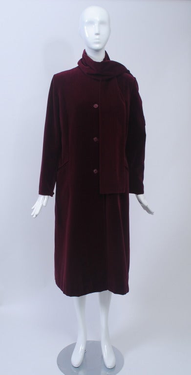 Burgundy velvet all-weather coat, single breasted, straight cut with slits on the sides and diagonal slit pockets. An attached scarf can be positioned in different ways.