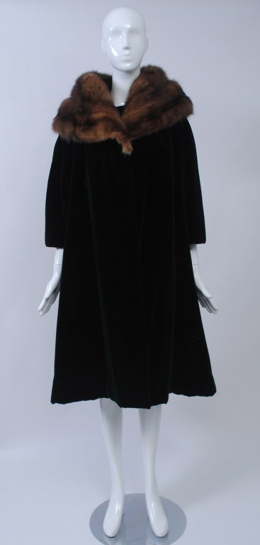 Evening coat and dress in forest green velvet trimmed in luxurious and full sable shawl collar. The swing coat has three-quarter sleeves and is interlinked for warmth. Underneath, the smilie sleeveless dress has a fitted bodice, boat neckline in