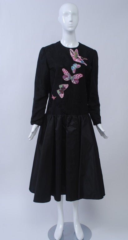 Hanae Mori evening dress of black silk, the bodice fashioned of a black-on-black butterfly design embellished with pastel beaded butterflies. Dropped waist, high neck, and long sleeves top a shirred skirt of plain silk taffeta that falls to mid